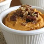 Pumpkin dip with cream cheese in small bowl topped with pecans.