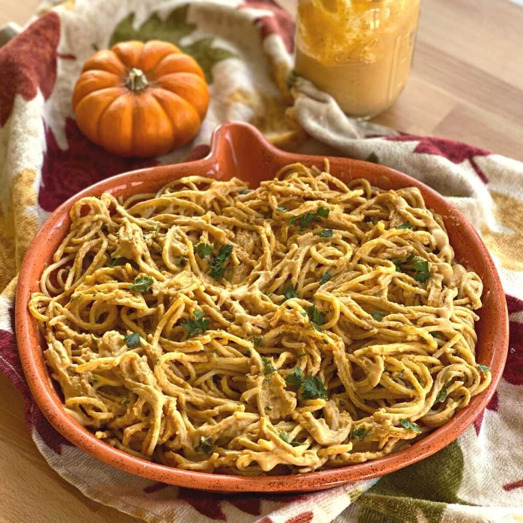 A vibrant bowl of spaghetti tossed in a creamy, orange-hued pumpkin sauce topped with fresh herbs.