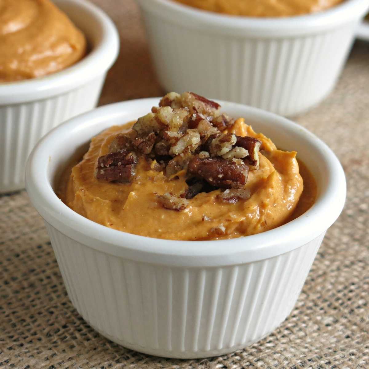 Pumpkin cream cheese dip in a serving cup topped with candied pecans.