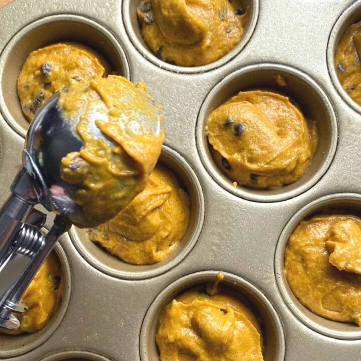 Scooping Greek yogurt pumpkin muffin batter into a muffin tin.
