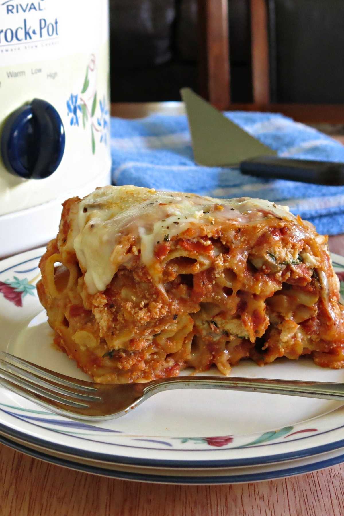 Serving of slow cooker baked ziti with crock-pot behind it.