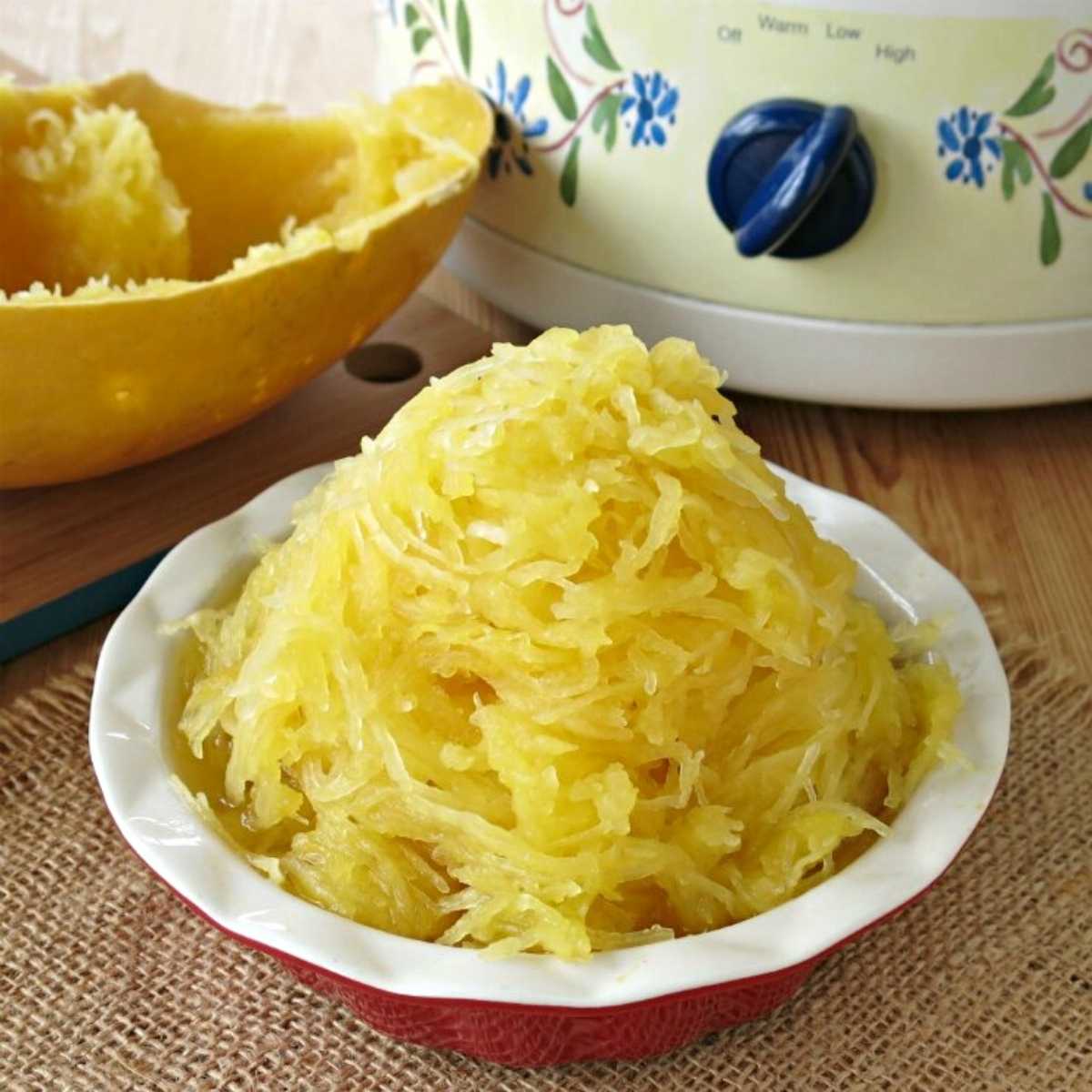 Strands of cooked spaghetti squash in a dish with a slow cooker behind it.