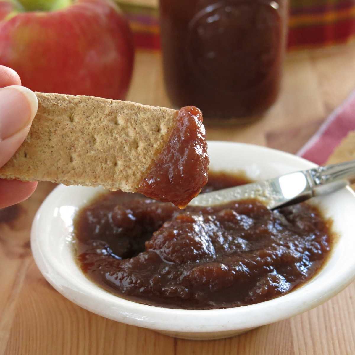Crock-pot apple butter with low sugar on a graham cracker with bowl below it. 
