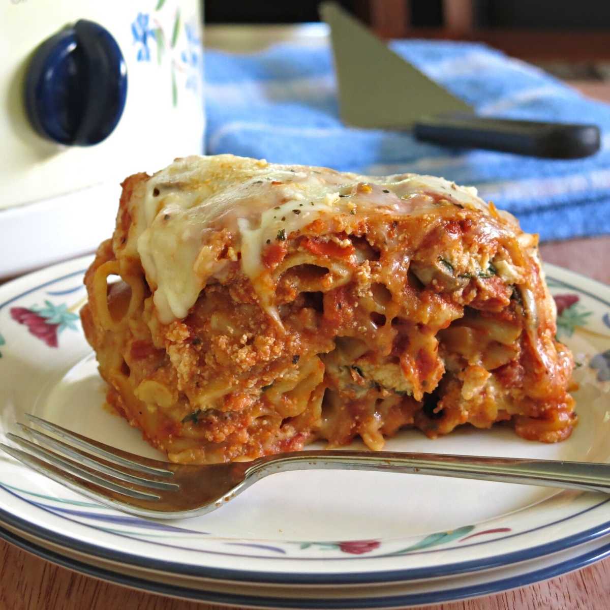 Serving of crock-pot baked ziti with ricotta in front of a slow cooker.