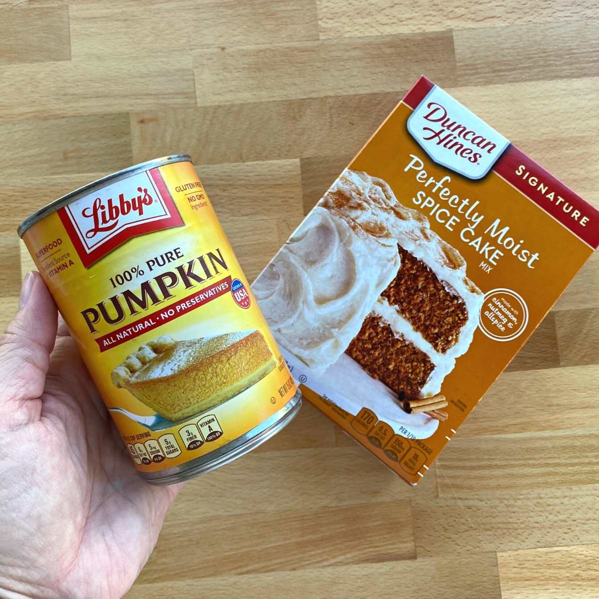 Hand holding a can of pumpkin puree and a box of Duncan Hines Spice Cake mix.