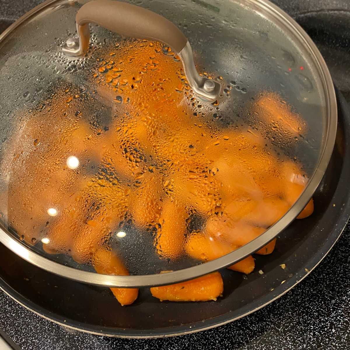 Partially covered skillet with baby carrots.