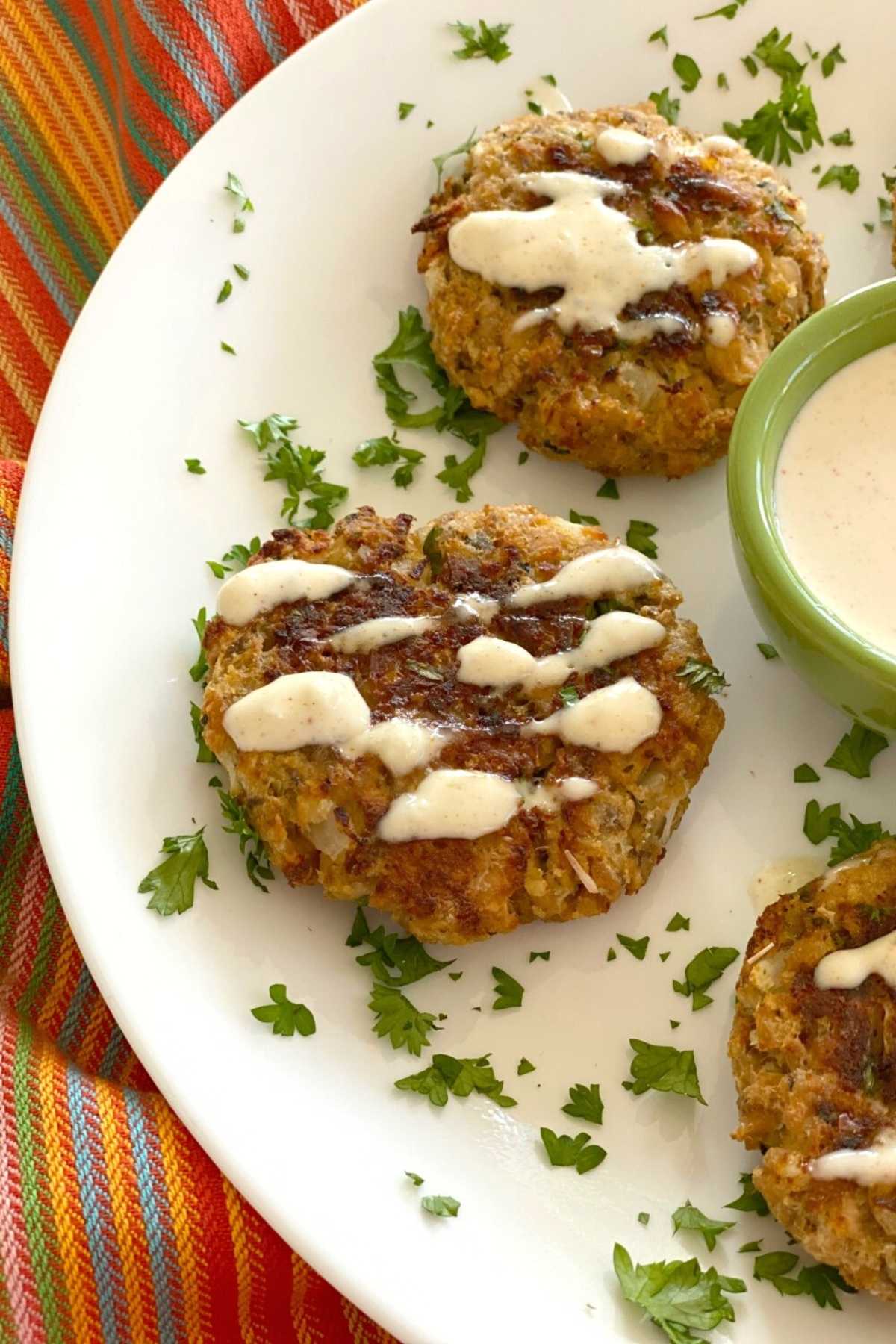 Three baked salmon patties drizzled with aioli on a plate with a bowl in the middle.