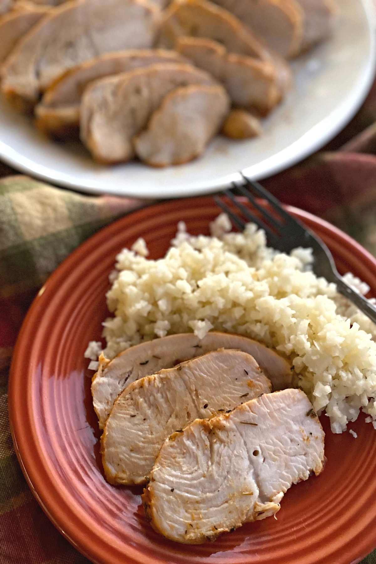 Baked turkey tenderloin on plate with cauliflower rice with platter of sliced turkey behind it.