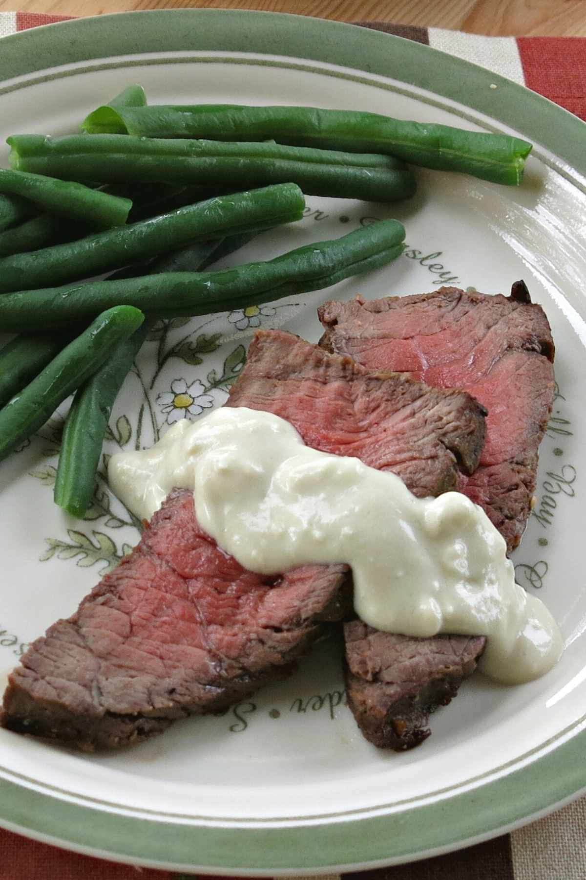 Easy blue cheese sauce drizzled over steak on a plate with green beans.