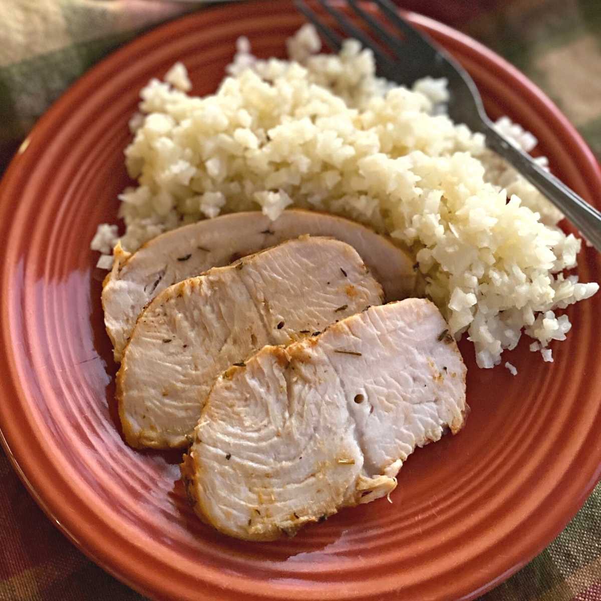 Three slices of turkey tenderloin on a plate with cauliflower rice and a fork.