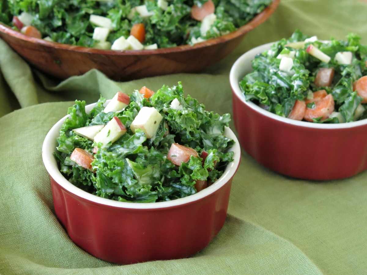 Two salad bowls with kale apple slaw with a larger bowl of it behind.