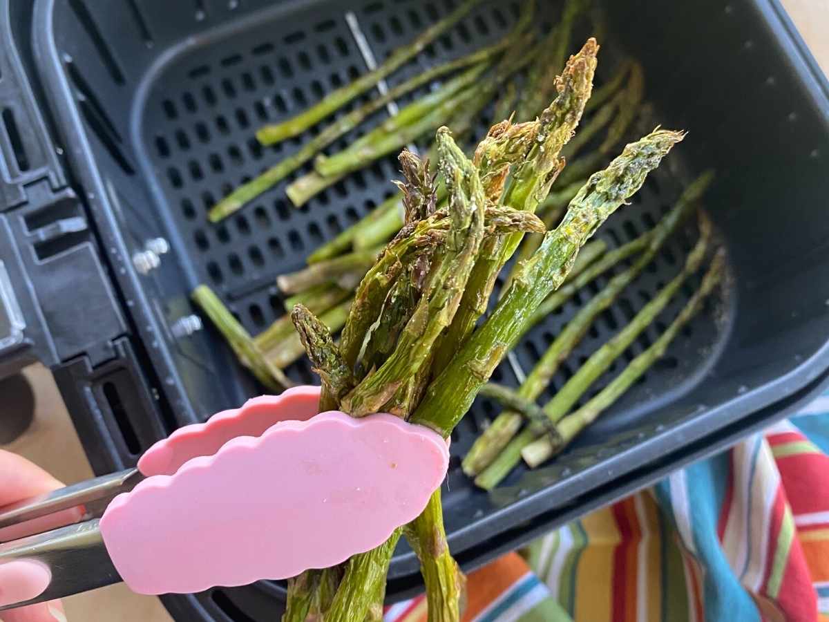 Tongs holding up roasted asparagus cooked in an air fryer.