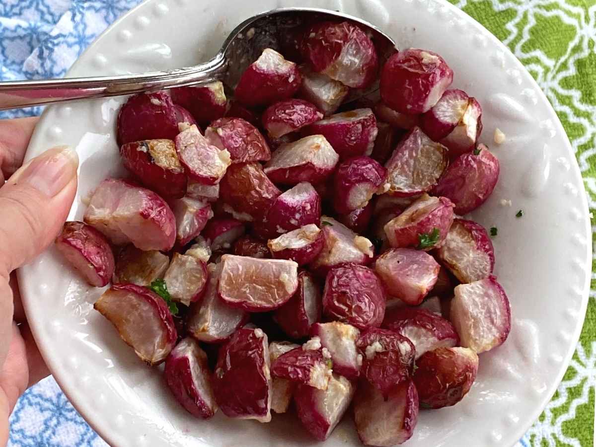 Hand holding bowl with roasted radishes.