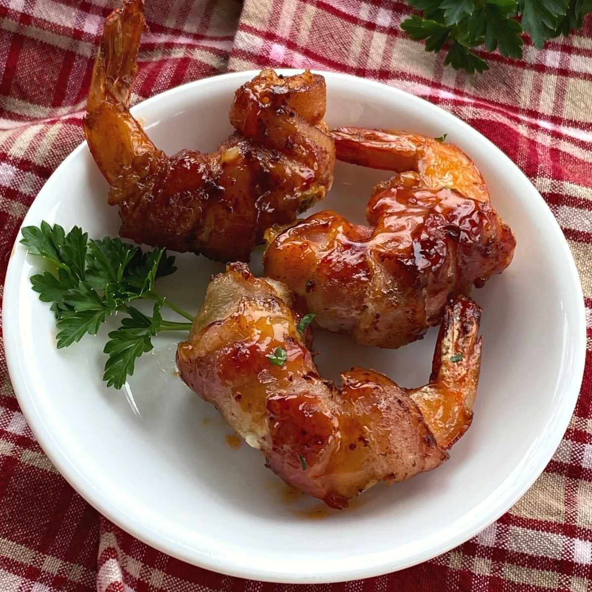 Three bacon wrapped shrimp stuffed with cream cheese and a jalapeno slice on a plate.
