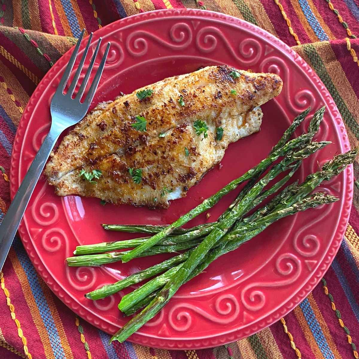 Blackened Cajun Catfish fillet on a plate with roasted asparagus.
