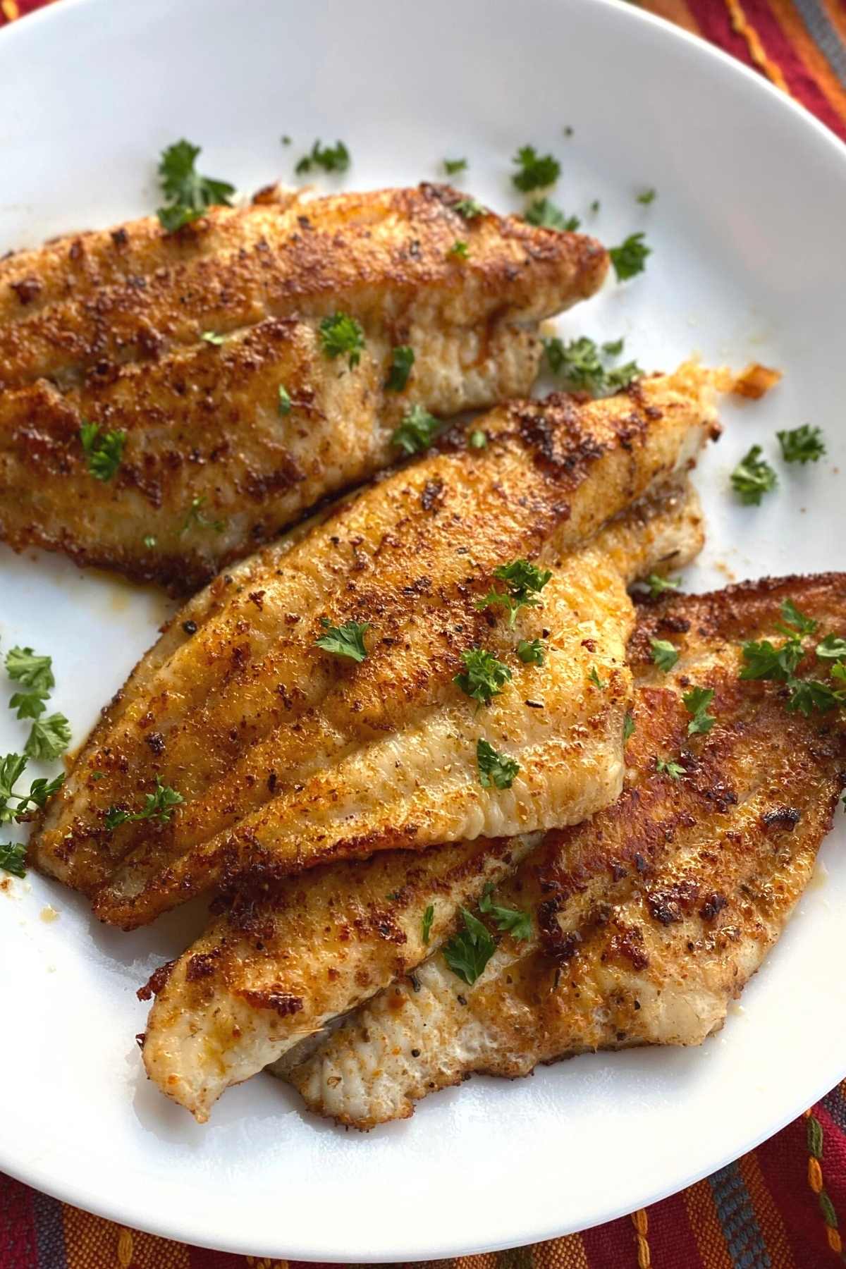 Cajun blackened catfish fillets on a plate sprinkled with parsley.