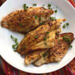 Three Cajun catfish filets on a plate.