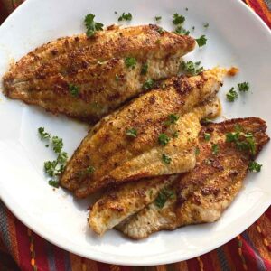 Three Cajun catfish filets on a plate.