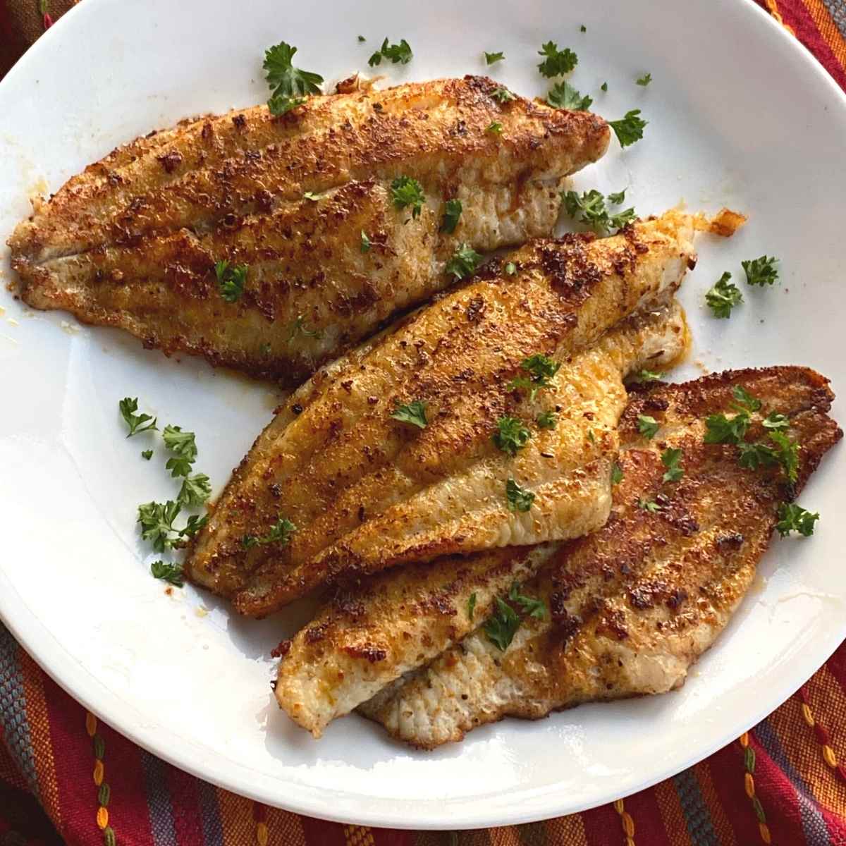 Three Cajun catfish fillets on plate.