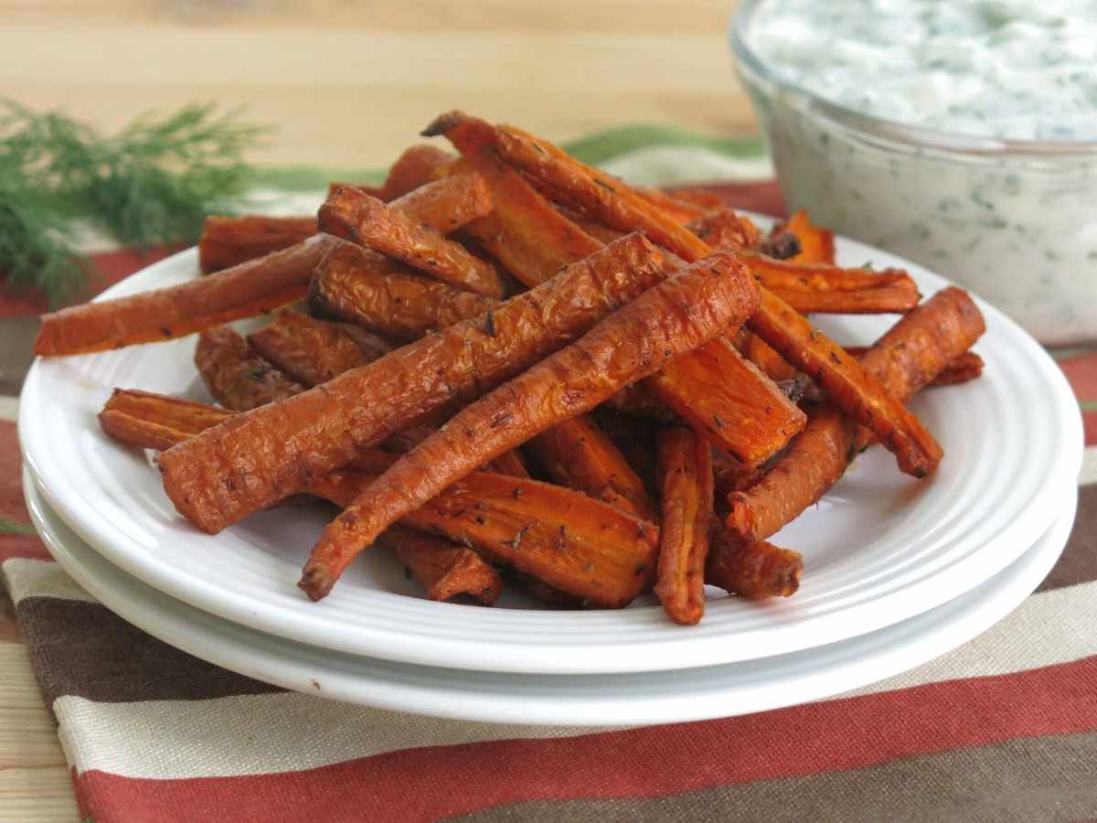 Carrot fries on a plate with yogurt dill dipping sauce behind it.