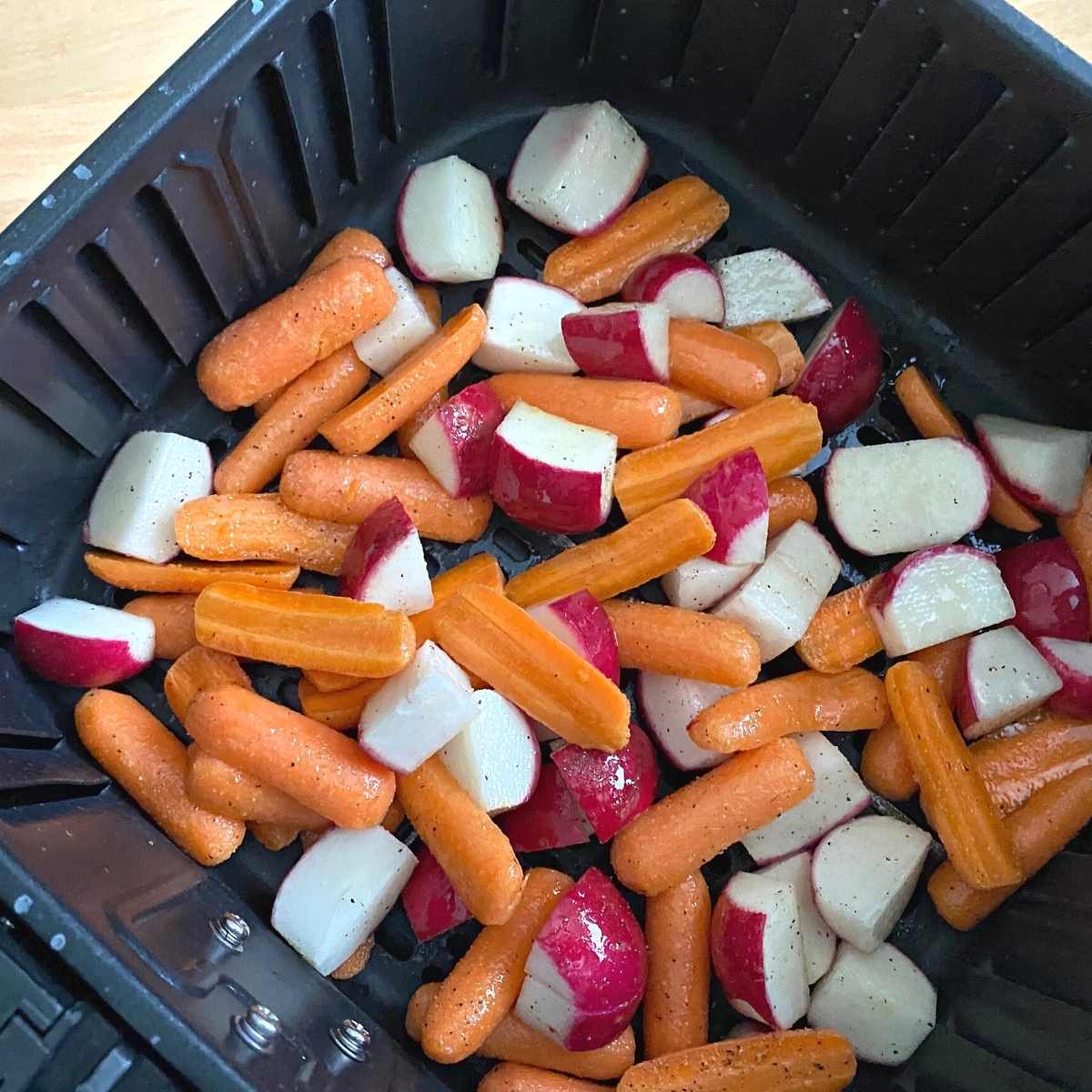 Carrots and radishes in an air fryer basket.