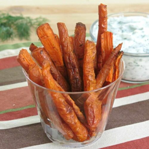 Carrot fries appetizer in a container with yogurt dipping sauce behind it.