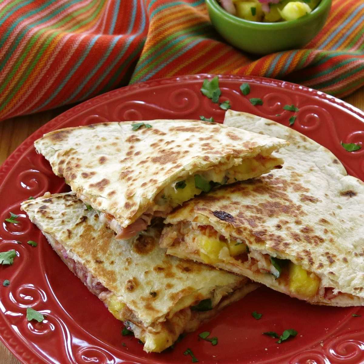 Hawaiian quesadilla with ham, pineapple, and cheese cut into triangles on a plate.