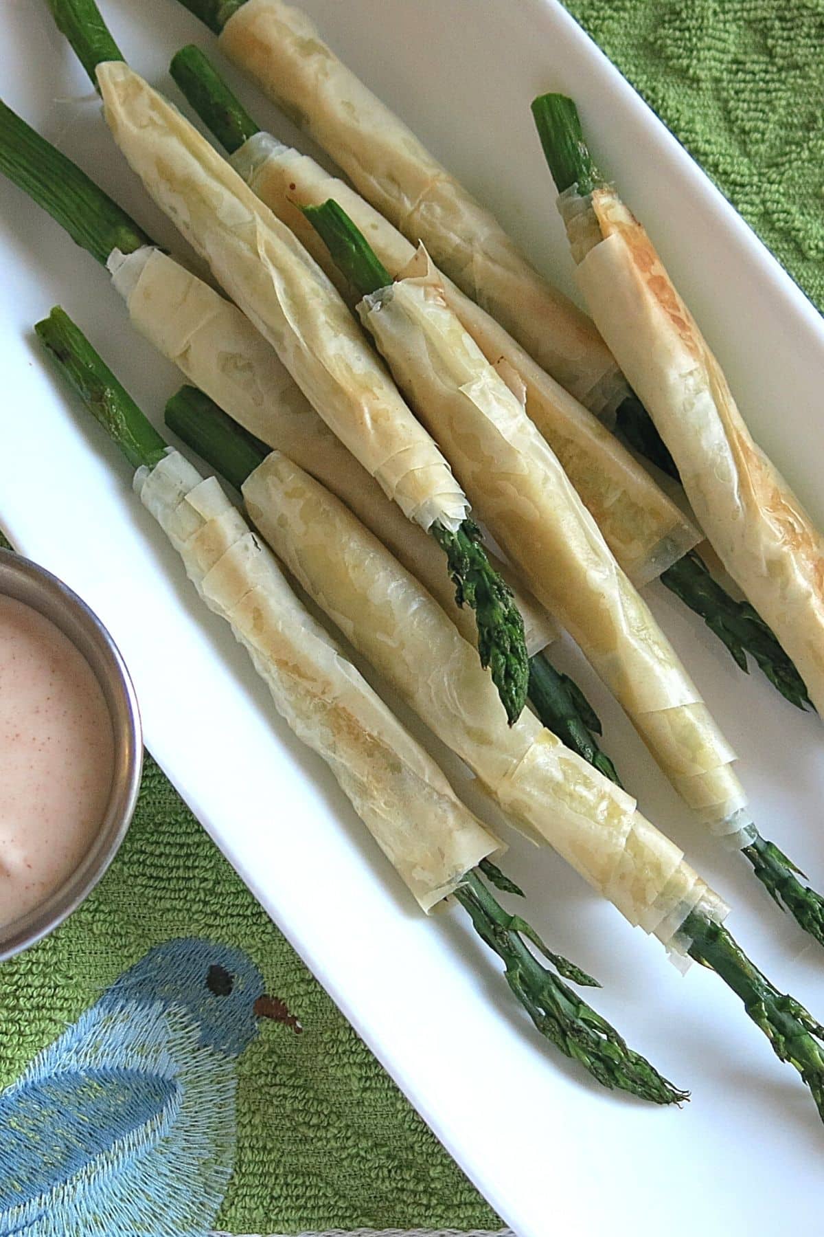 Phyllo wrapped asparagus on a platter next to aioli dipping sauce.