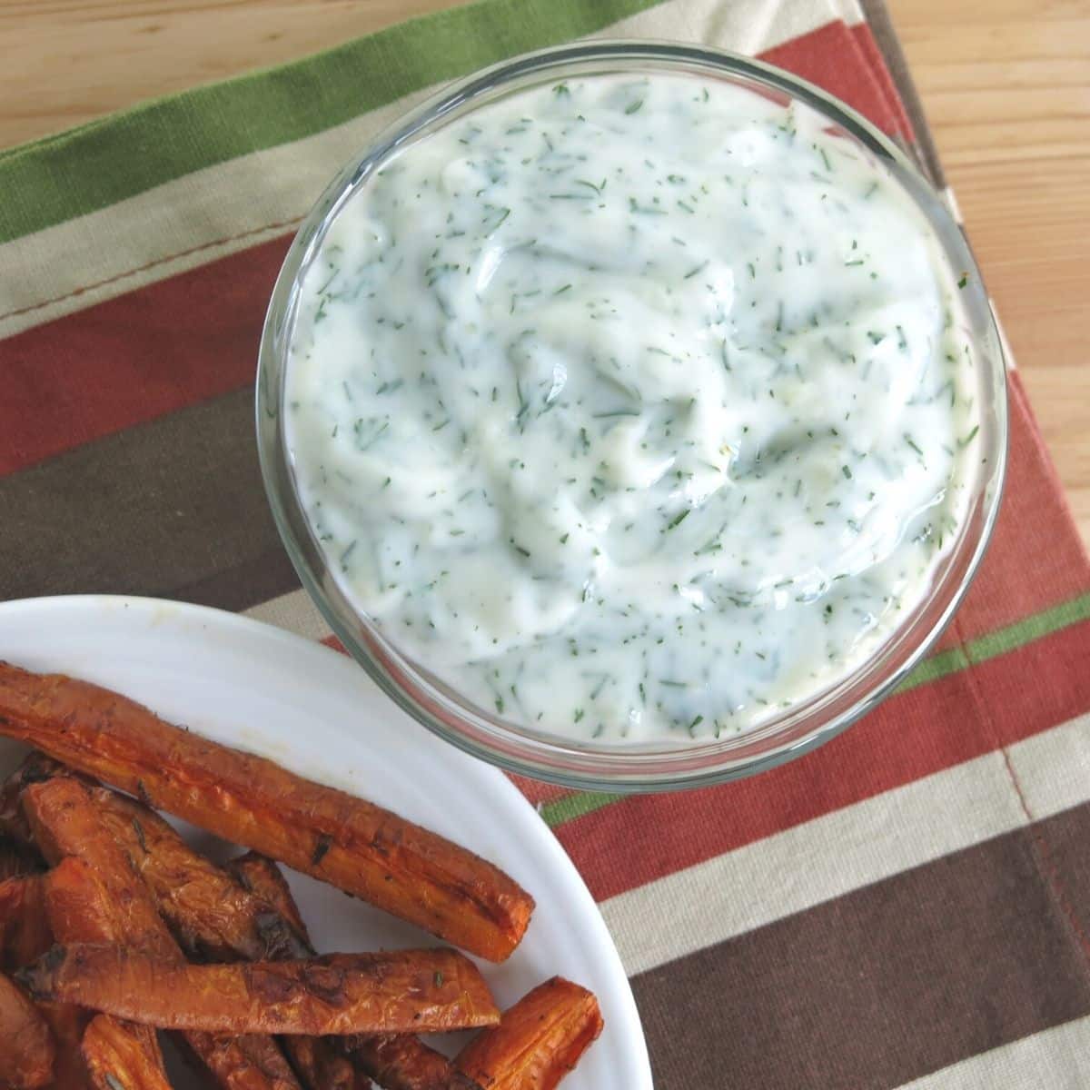 Yogurt dipping sauce in a bowl next to a plate of healthy carrots fries.