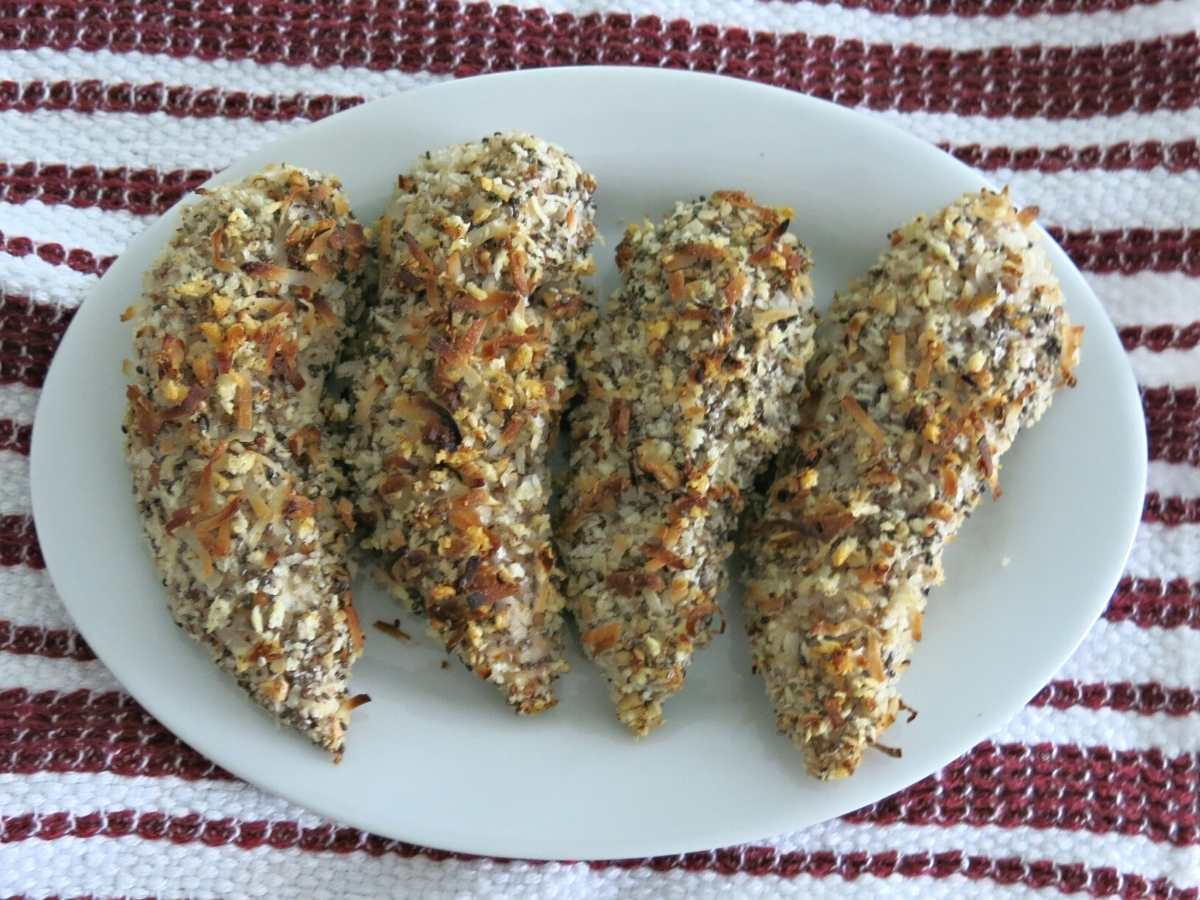 Four crispy baked chicken fingers in a row on a plate.