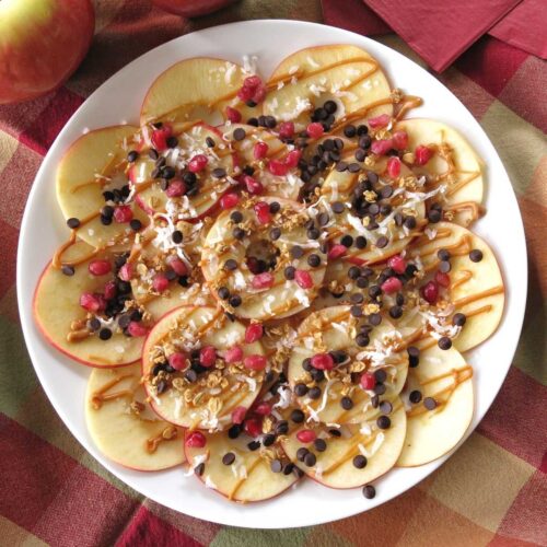 Healthy apple nachos topped with almond butter, granola, chocolate chips, and coconut on a plate.