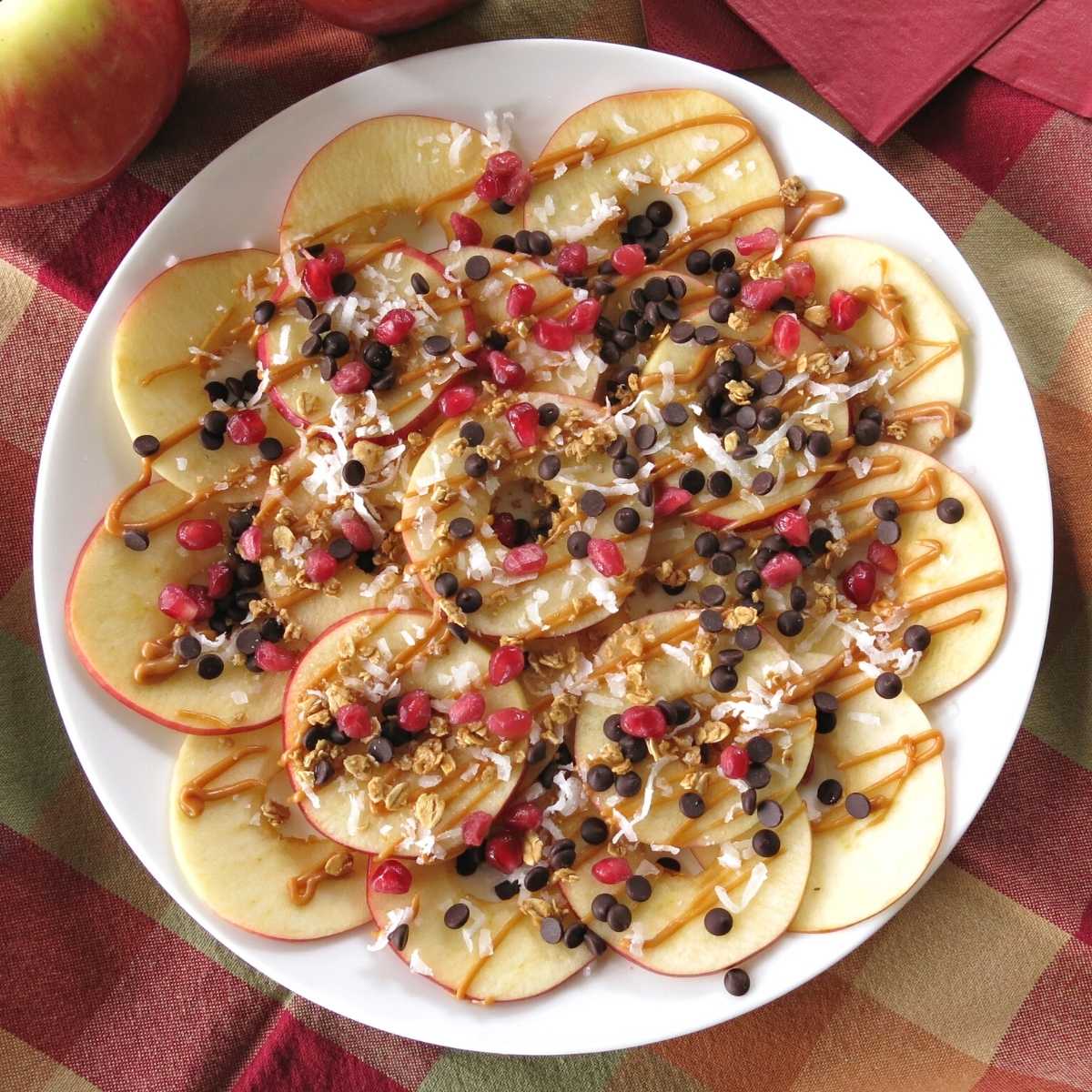 Plate of healthy apple nachos topped with almond butter, granola, chocolate chips, coconut flakes, and pomegranate seeds.