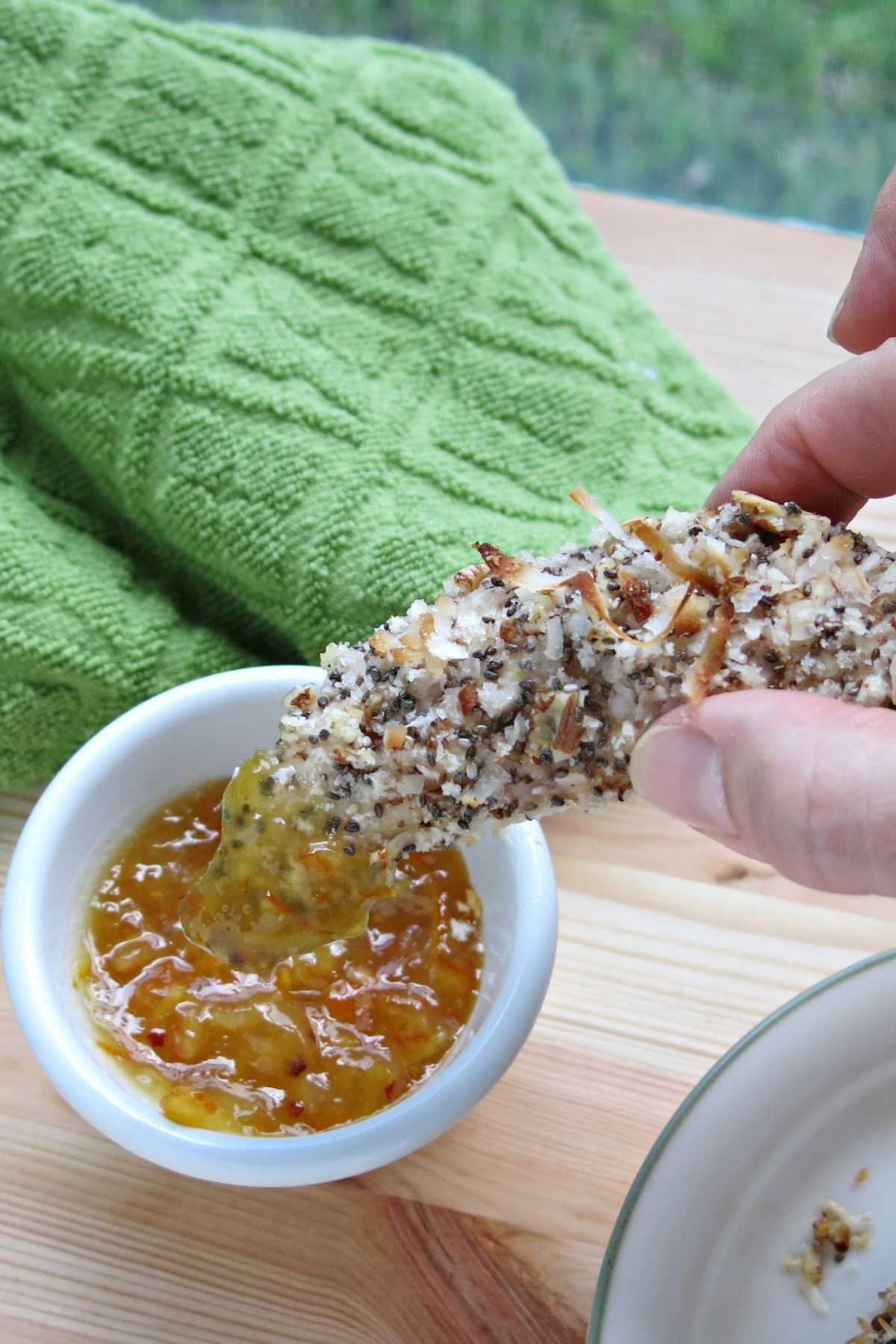 Fingers holding a easy baked chicken tender that has been dunked into a sauce.