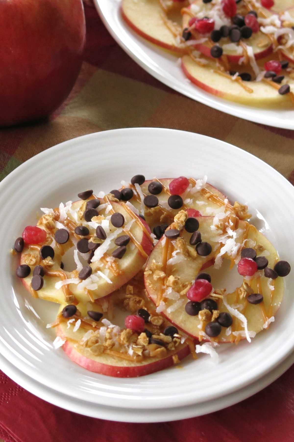 A serving of loaded apple nachos drizzled with nut butter and topped with granola, chocolate chips, coconut on a plate.