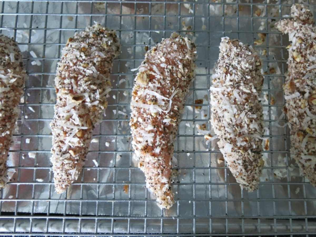 Uncooked chicken tenders with panko breading on a cooling rack placed on top of a baking sheet.