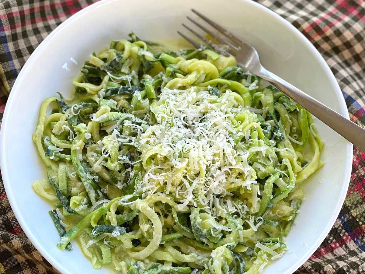 Zucchini noodle alfredo topped with grated Parmesan cheese in a bowl with a fork.