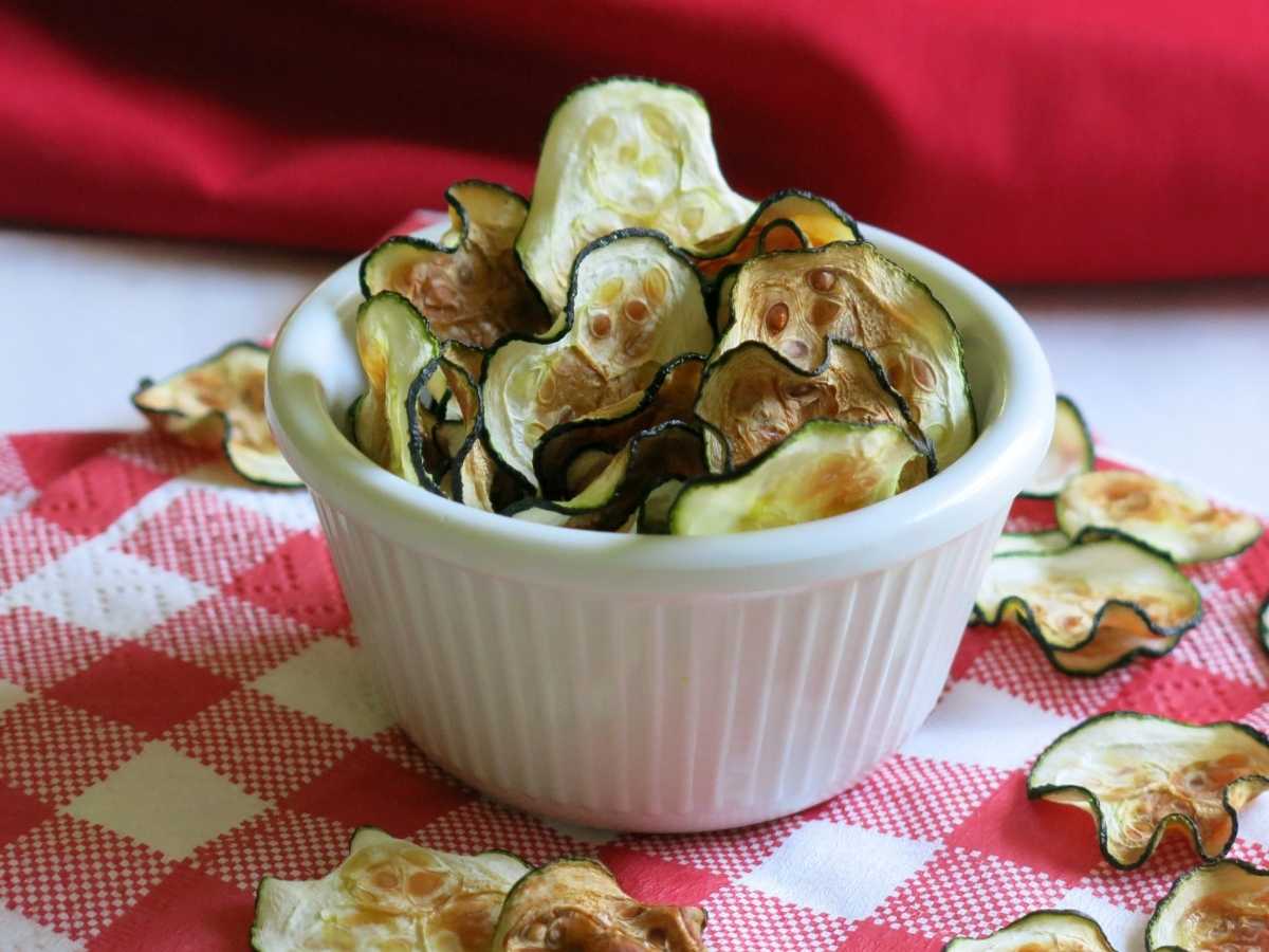 Zucchini chips standing in a serving cup with more on the napkin below.