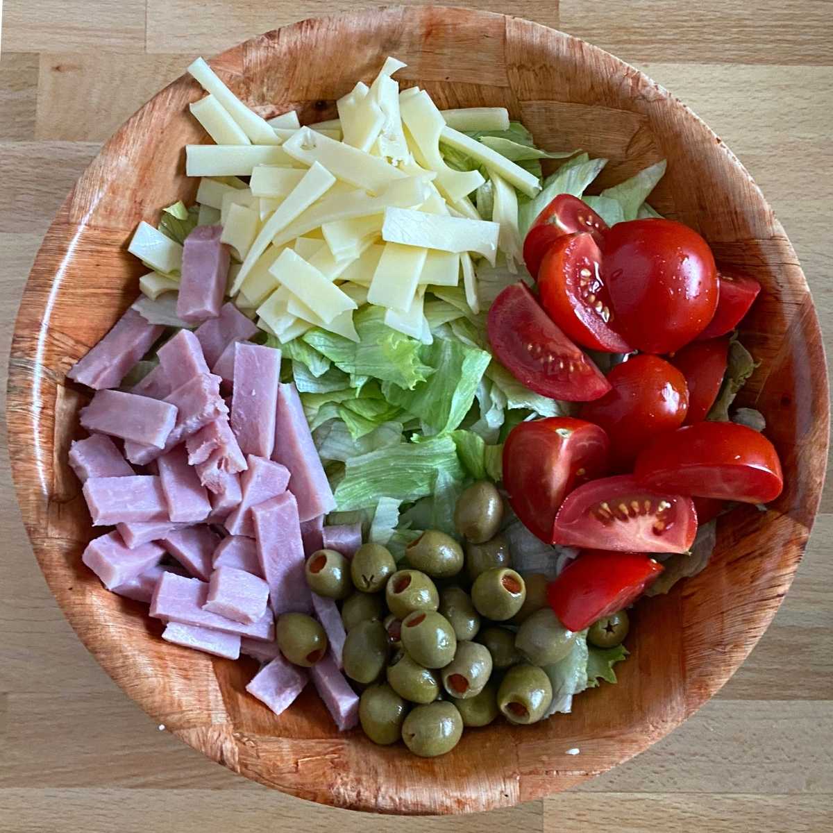 Julienned Swiss cheese and ham, wedges of tomato, green olives and lettuce in a bowl.