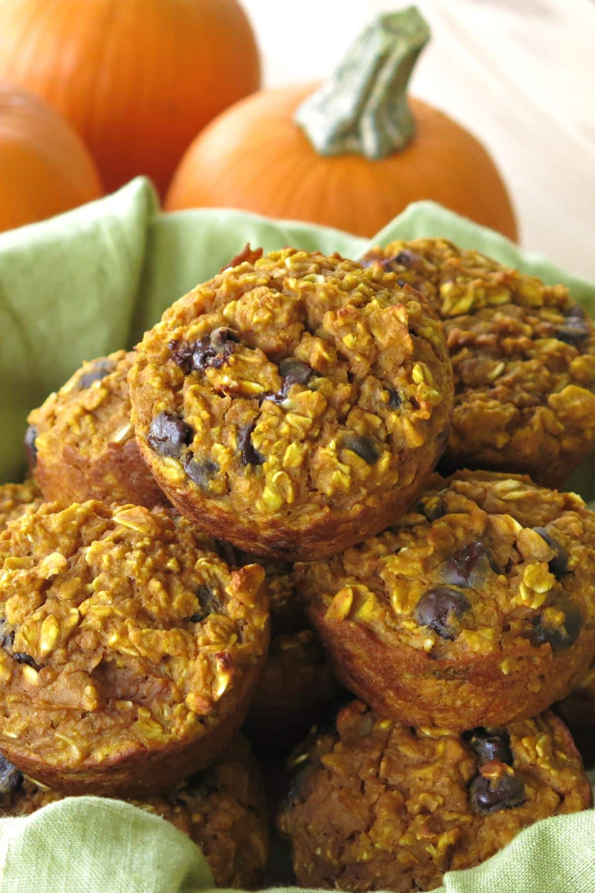 Baked oatmeal pumpkin cups piled on top of each other with pumpkins behind them.