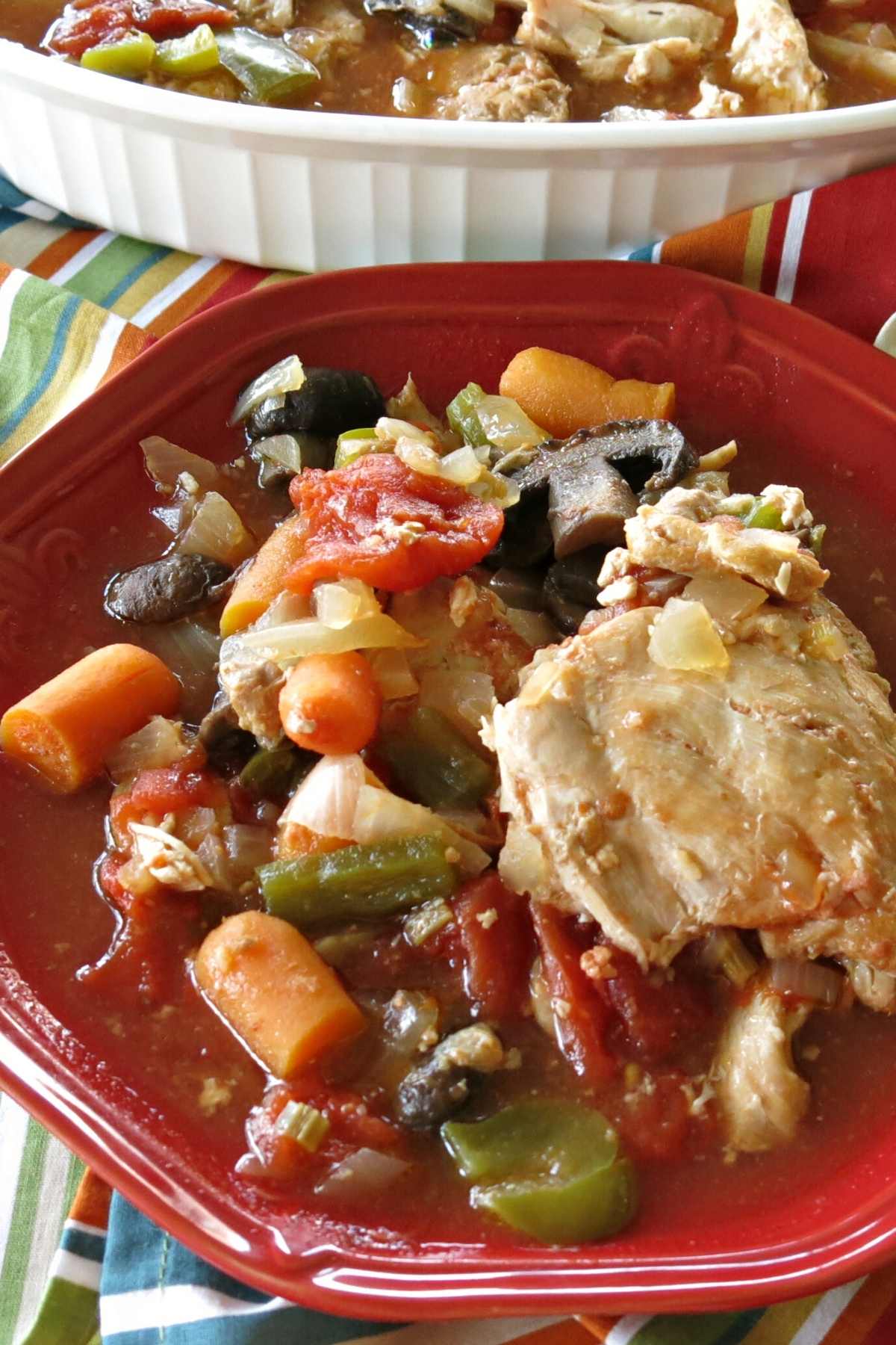 Slow Cooker Chicken and Stewed Tomatoes on a plate with a platter behind it.