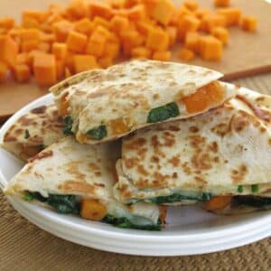 Butternut squash quesadilla cut into triangles on a plate with squash cubes behind it.