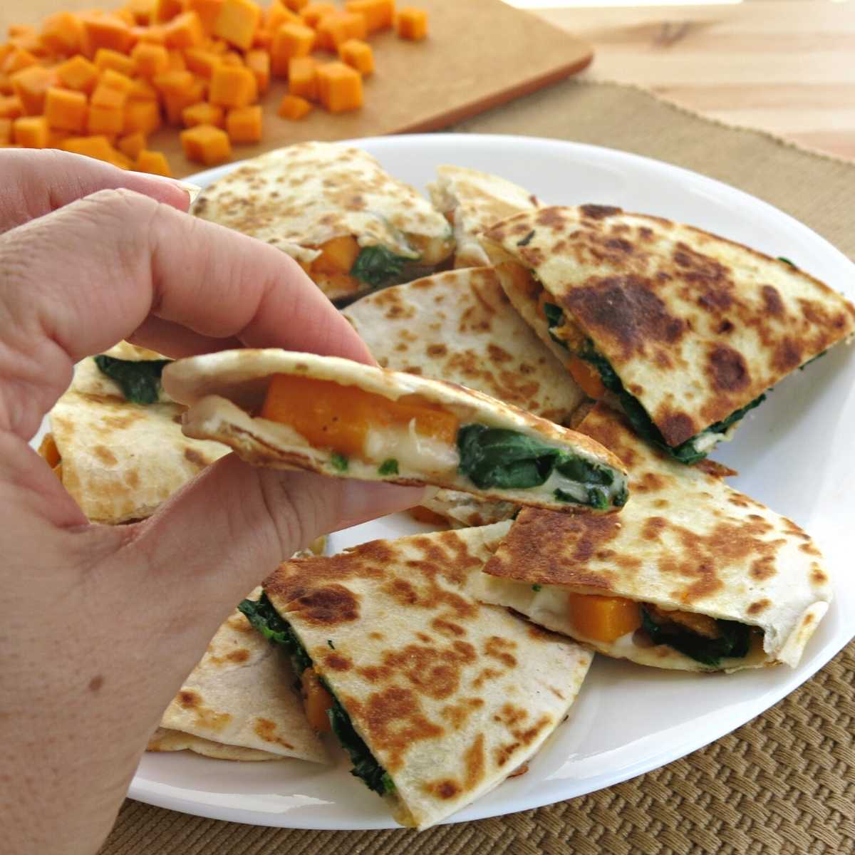 Hand holding a a triangle of a butternut squash quesadilla with spinach.