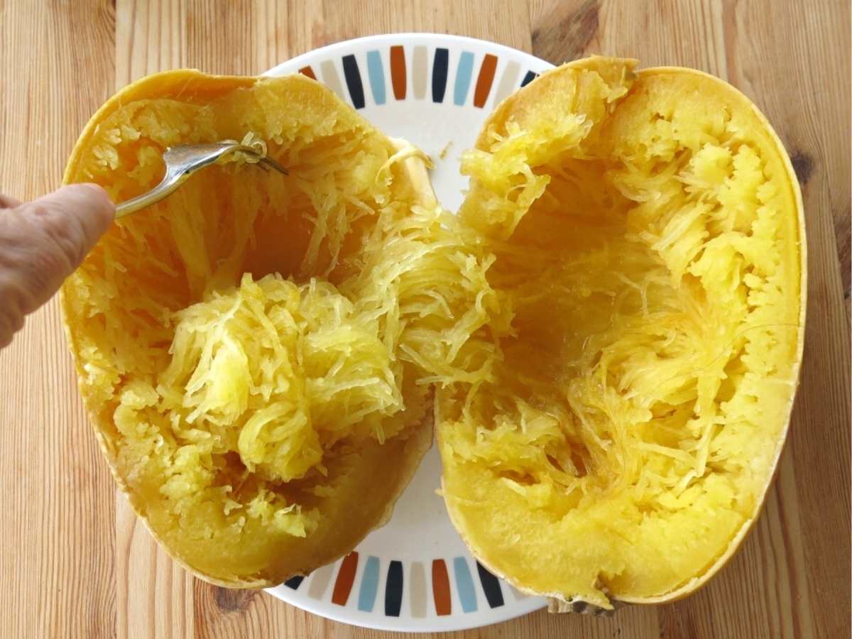 Fork removing strands from cooked spaghetti squash that has been cut in half.