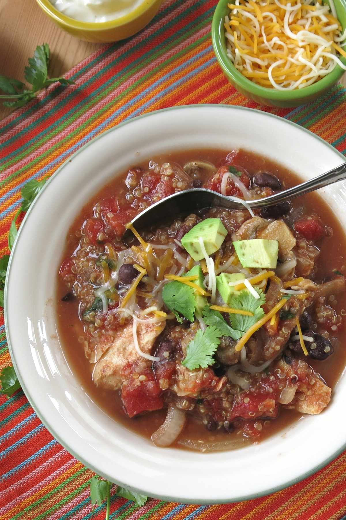 Crock-pot chicken quinoa taco soap in bowl with toppings behind it.