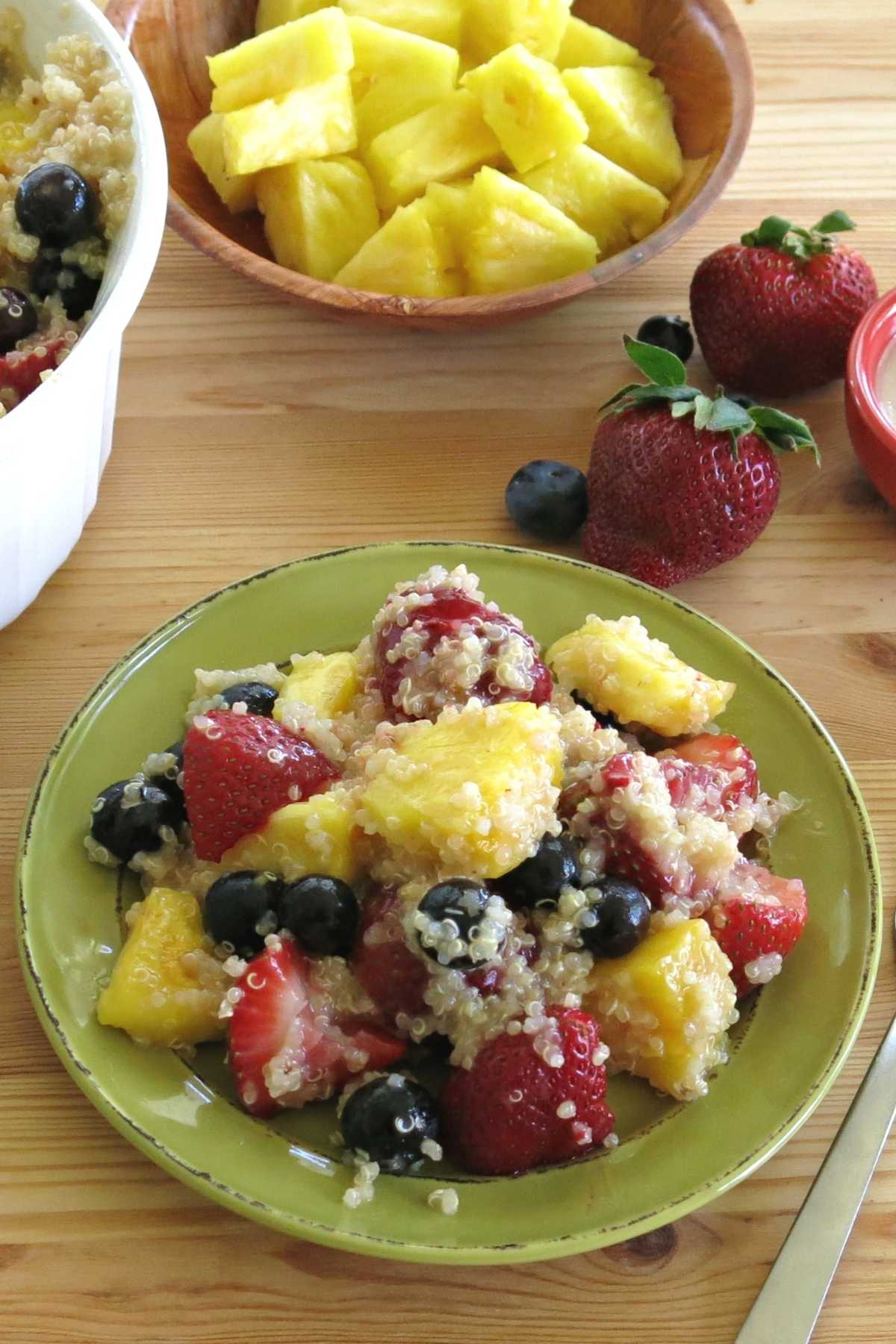 Fruit salad with blueberries, strawberries, pineapple, and quinoa on a plate with ingredients in the background.