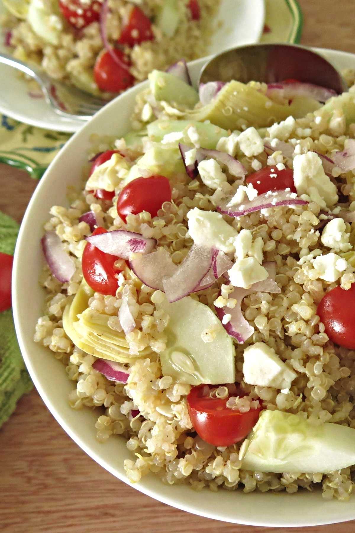 Greek quinoa salad with artichokes, cucumbers, grape tomatoes, and onions in a large serving bowl.