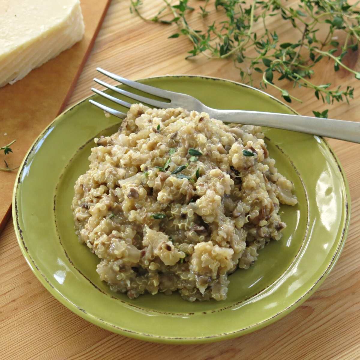 Cheesy mushroom quinoa on a plate with Parmesan cheese and thyme in the background.