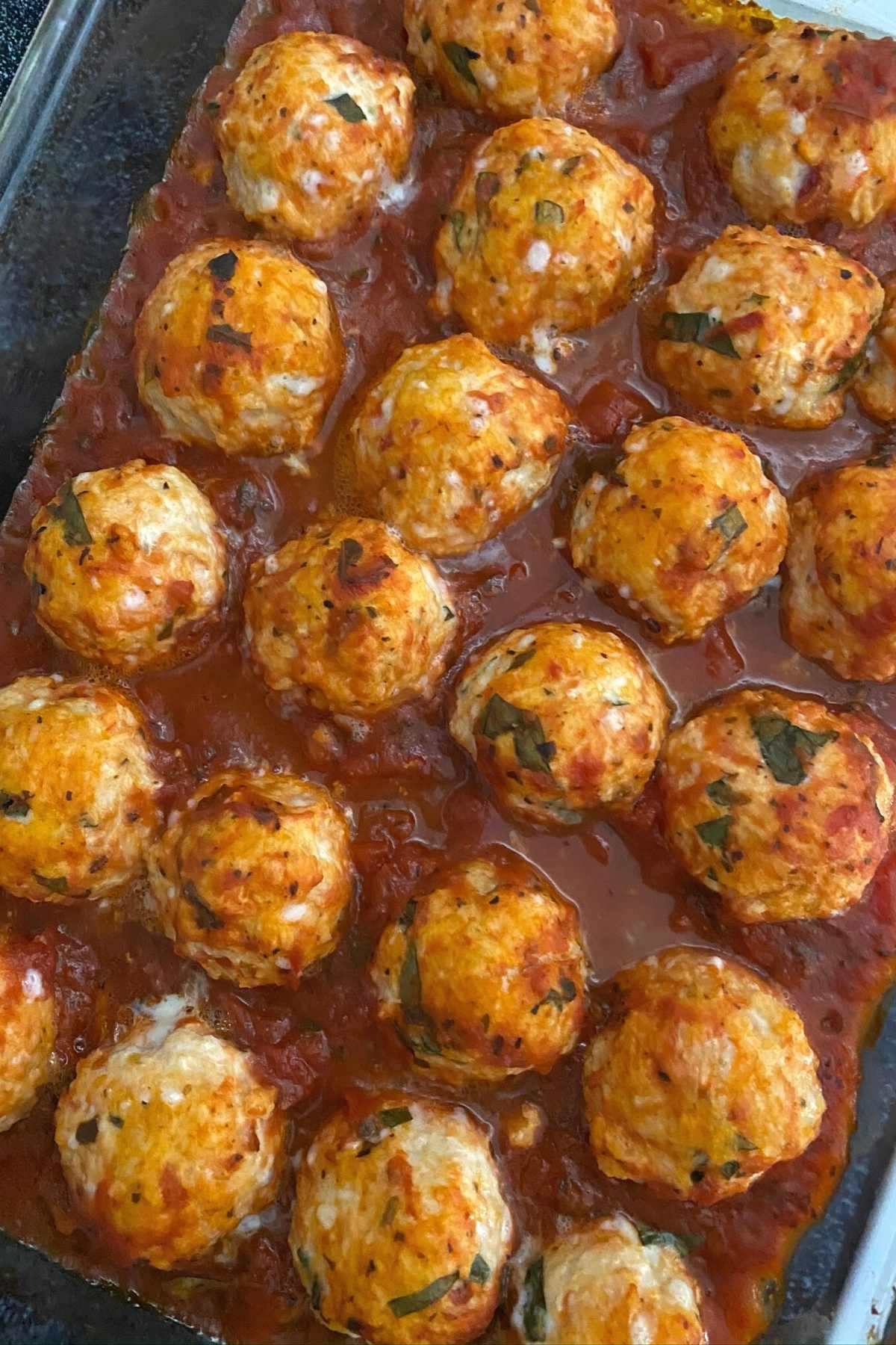 Cheesy baked ground chicken parmesan meatballs in a glass baking dish.