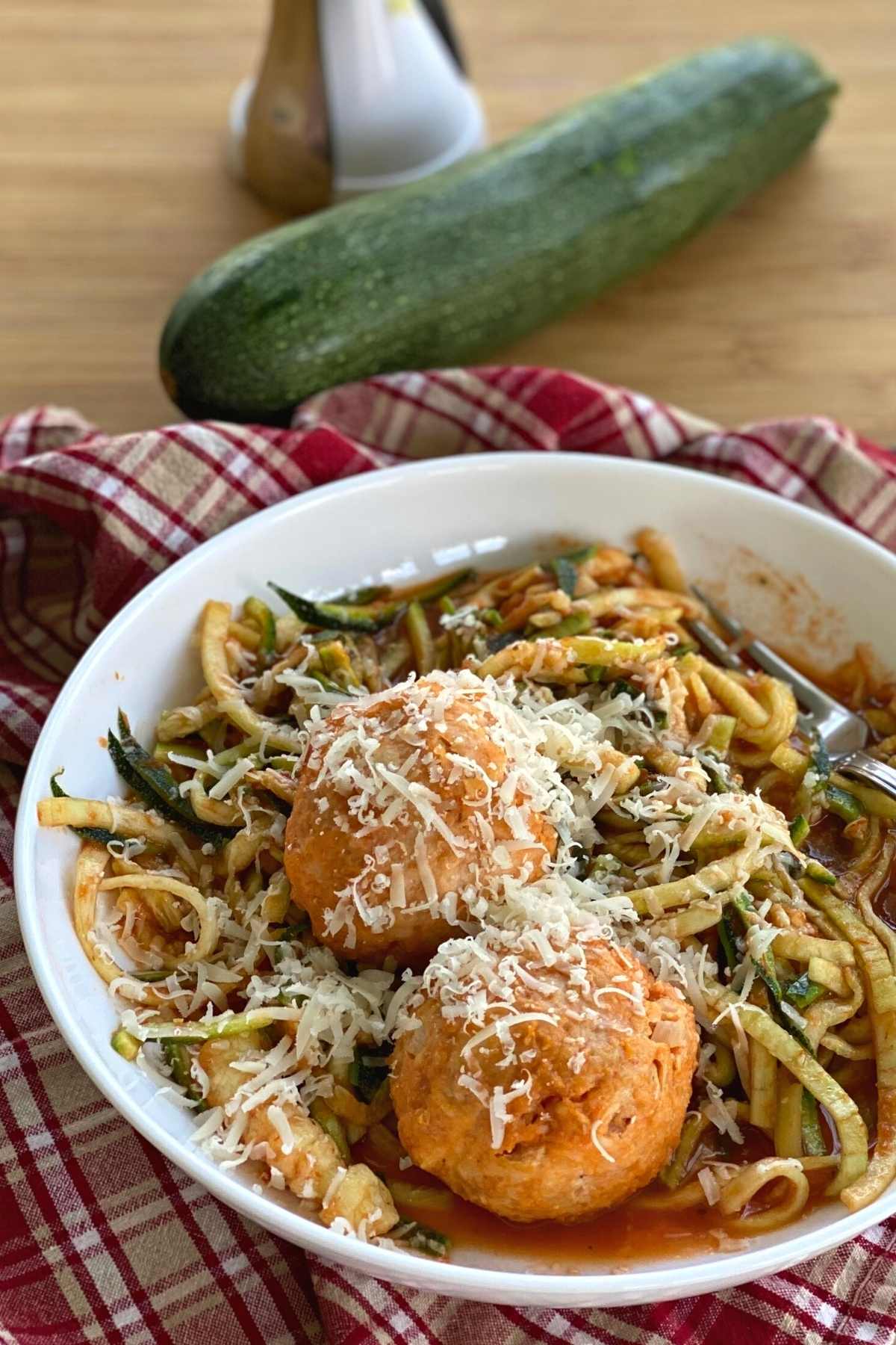 Chicken Parmesan meatballs in a bowl over zucchini noodles coated with spaghetti sauce and topped with more cheese.