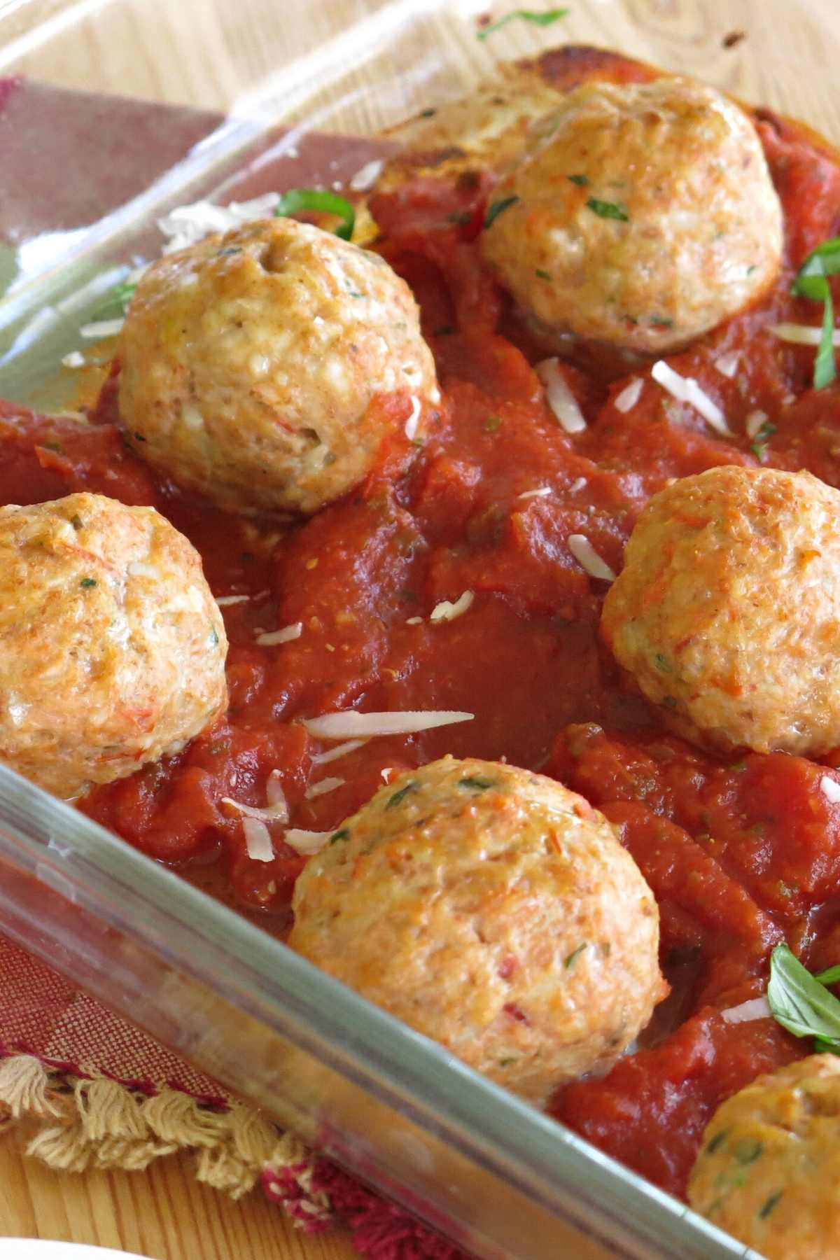 Chicken parm meatballs in a glass baking dish on top of marinara sauce.